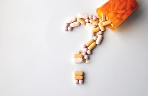 different drug and health supplement pills in a question mark